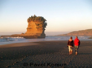 Две девушки прогуливаются по темному песку пляжа Попрорари возле скалы "Башмак великана" 