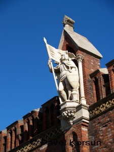 Белая статуя рыцаря с флагом и щитом над древними воротами