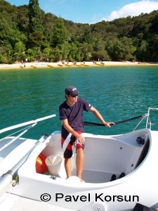 Молодой яхтсмен на борту катамарана возле берега на котором группа туристов на каяках