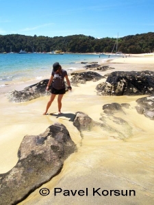Девушка на пляже с серебристым песком и черными камнями в заливе Анкоридж Бэй