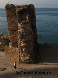 Мужчина идет возле разрушенной башни крепости в Синопе и пара смотрит на Черное море