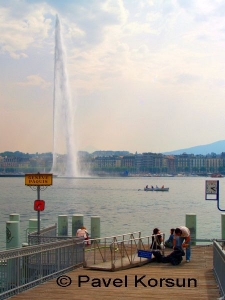 Фонтан в Женеве вздымающийся на огромную высоту, лодка плывущая по Женевскому озеру и люди на причале