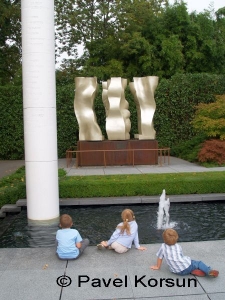Трое детей возле фонтана смотрят на три вращающиеся фигуры атлетов